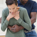 Nella foto c'è un ragazzo che esegue la manovra di Heimlich ad una ragazza che si tiene la gola fra le mani ad indicare che sta soffocando