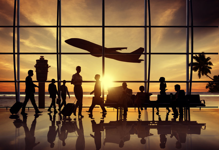 Nella foto è riprodotto l'interno di un aeroporto dove ci sono controluce rispetto ad un finestrone tanti passeggeri in attesa e in transito. dietro la finestra, sempre in controluce, si staglia la sagoma di una aereo che sta decollando