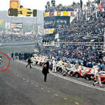 Jacky Ickx alla partenza della corsa delle 24 ore di Le Mans del 1969. Jacky, evidenziato da un cerchio rosso, passeggia verso la sua monoposto schierata dall'altro lato della pista. Sullo sfondo tribune piene di spettatori.