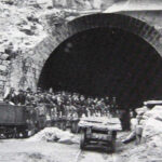 Foto in bianco e nero scattata nel 1875 all'ingresso del tunnel del Gottardo. Molti lavoratori sono stipati sui carrelli che portano in galleria